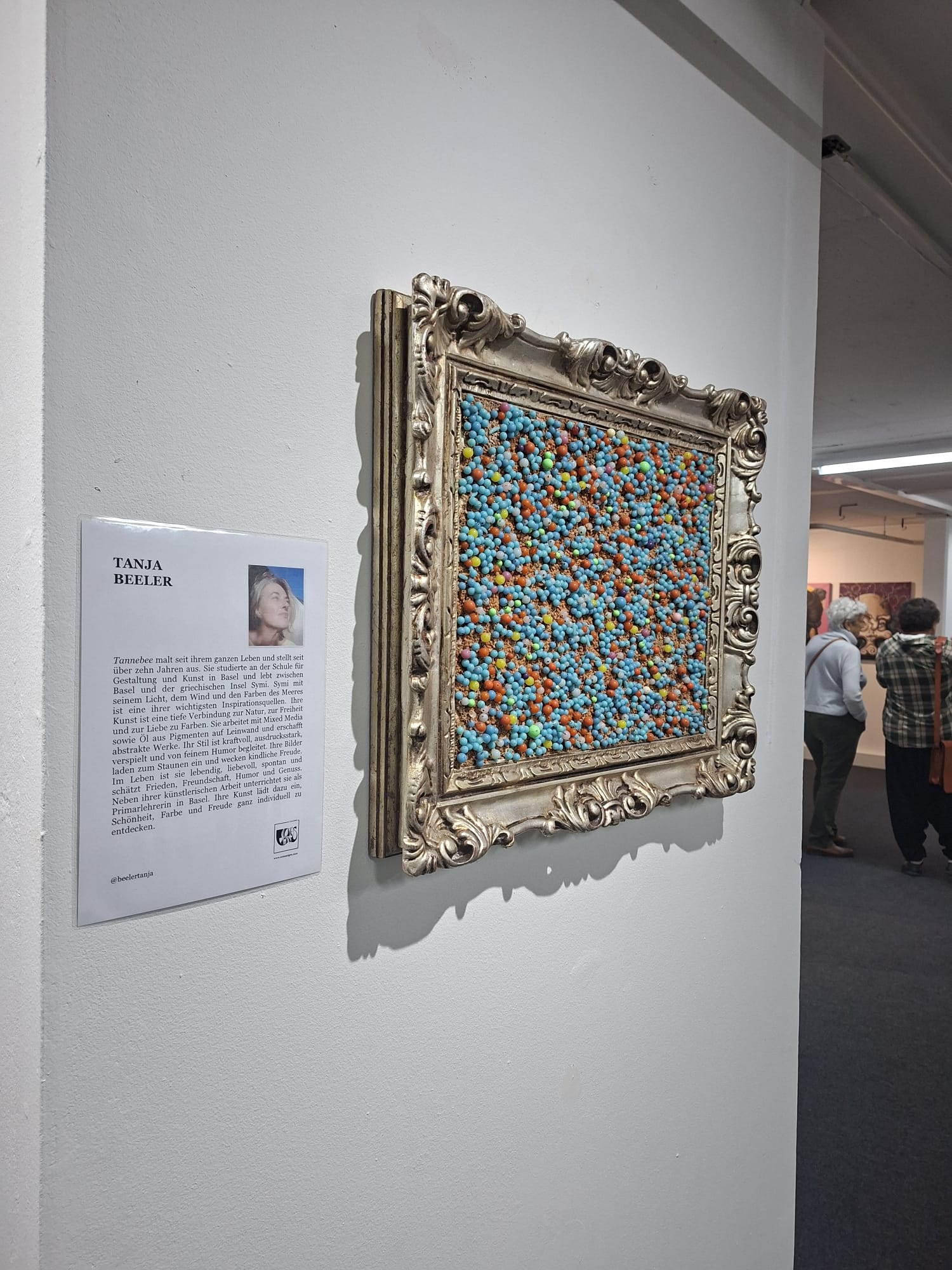 Ausstellungsansicht ART FRIENDS im BaselArtCenter: Werk im verzierten Rahmen neben der Künstlerbeschreibung von Tanja Beeler