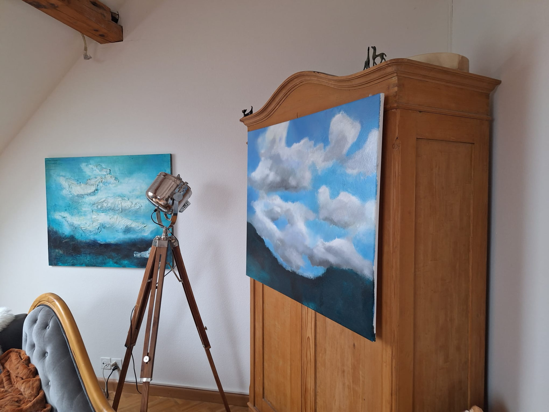 Ausstellungsansicht im Atelier: Bild mit blauem Himmel und weissen Wolken vor einem alten Holeschrank