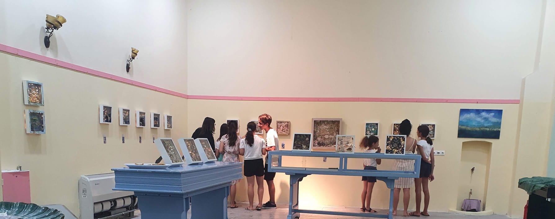 Ausstellungsansicht im Gemeindehaus Symi: Besucherinnen und Besucher betrachten die ausgestellten Arbeiten